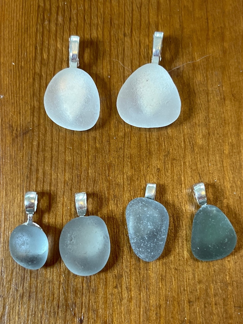Op de afbeelding: Zes  zee-glas hangers met zilveren springringen. Twee zijn helder, twee zijn wit en twee zijn groen.