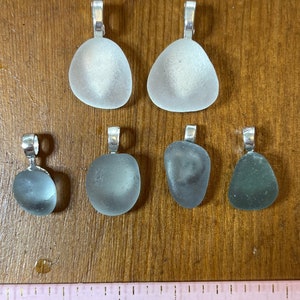Op de afbeelding: Zes  zee glas hangers met zilveren beugel, twee zijn helder, twee zijn lichtblauw en twee zijn donkerblauw.