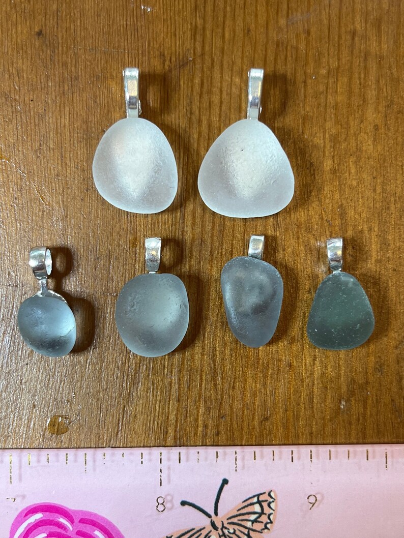 Op de afbeelding: Zes  zee glas hangers met zilveren beugel, twee zijn helder, twee zijn lichtblauw en twee zijn donkerblauw.