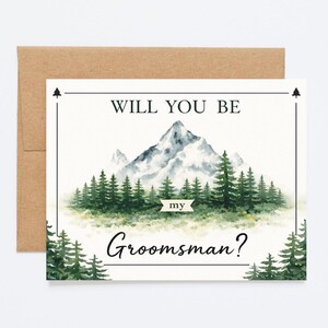 May include: A watercolor-style greeting card with a mountain and forest scene. The text reads "WILL YOU BE my Groomsman?" The card is white with a brown envelope behind it.