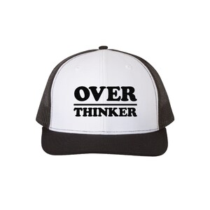 May include: A white and black trucker hat with the words "OVER THINKER" in bold, black capital letters. The hat has a black brim and a mesh back, offering a classic, casual style.