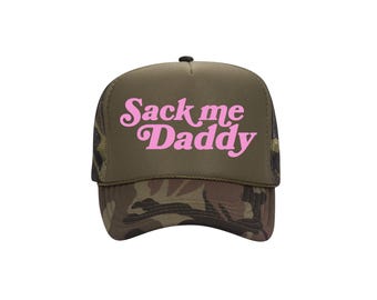 Könnte beinhalten: Trucker-Cap mit Camouflage-Schirm und Mesh-Rückseite. Die Frontplatte ist olivgrün mit den Worten "Sack me Daddy" in rosa Schrift. Die Kappe hat einen schwarzen Knopf oben.