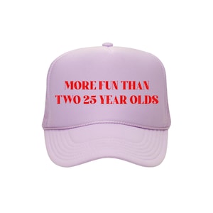 May include: A light purple trucker hat with the text "MORE FUN THAN TWO 25 YEAR OLDS" in red block letters. The hat has a mesh back and a curved brim.