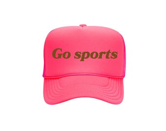 Könnte beinhalten: Leuchtend pinkfarbene Trucker-Cap mit dem Schriftzug "Go sports" in brauner Schrift auf der Vorderseite. Die Kappe hat einen Mesh-Rücken und einen gebogenen Schirm. Ein lustiges Accessoire für Sportfans.