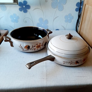 Könnte beinhalten: Zwei antike Kochgeschirre mit Blumendesigns. Ein brauner und weißer Topf mit Deckel und eine braune und weiße Bratpfanne mit Griff.