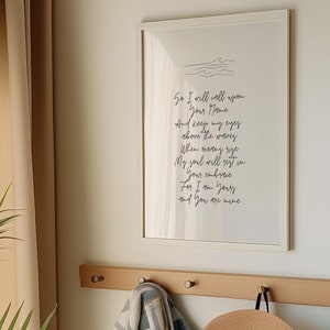 Op de afbeelding: Een wit ingelijst print met een handgeschreven gedicht over liefde en thuis. De print hangt aan een muur met een houten kapstok eronder. De kapstok heeft een geruit deken, een strohoed en een witte draagtas eraan.