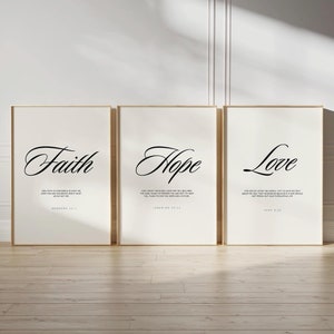 May include: Three framed art prints with the words "Faith," "Hope," and "Love" in elegant black script. Each print includes a related Bible verse in a smaller font. The frames are a light brown color, and the background is a neutral off-white.