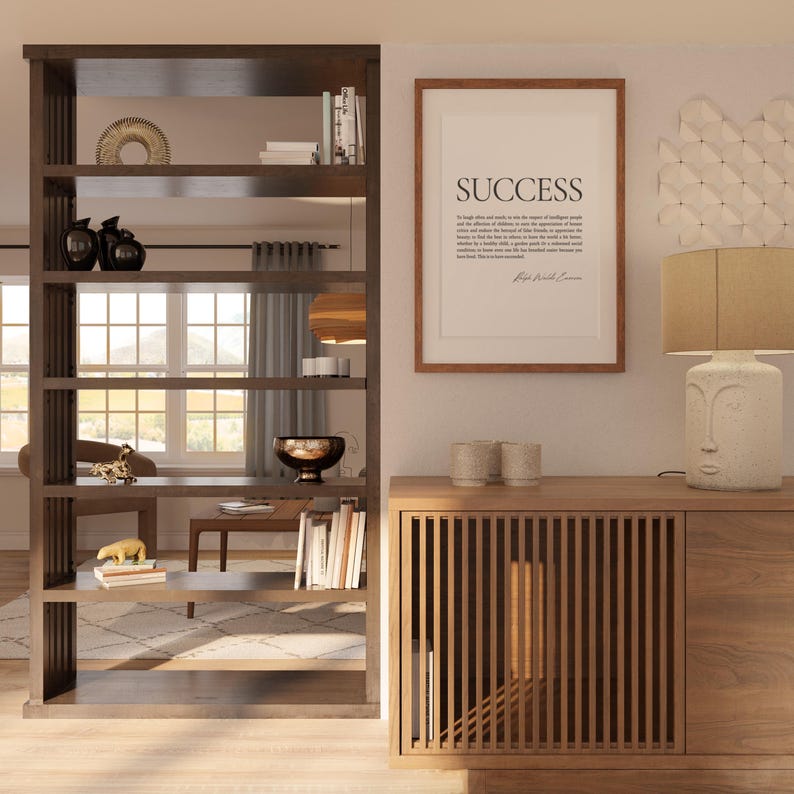 May include: A wooden room divider with five shelves, displaying various decorative objects, including a bowl, books, and a gold animal figurine. The divider is next to a wooden cabinet with a slatted front and a solid wood door. A framed print with the word "SUCCESS" and a quote by Ralph Waldo Emerson is hanging on the wall above the cabinet. A lamp with a beige shade and a face-shaped base sits on top of the cabinet.
