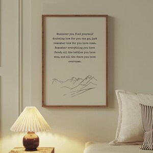 May include: A motivational quote printed on a framed poster with a simple line drawing of mountains at the bottom. The quote reads: "Whenever you find yourself doubting how far you can go, just remember how far you have come. Remember everything you have faced, all the battles you have won, and all the fears you have overcome."