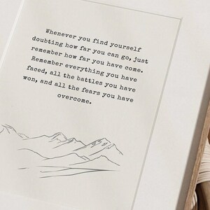 May include: A motivational quote about overcoming challenges and remembering how far you've come. The quote is printed in black text on a white background with a simple line drawing of mountains at the bottom.