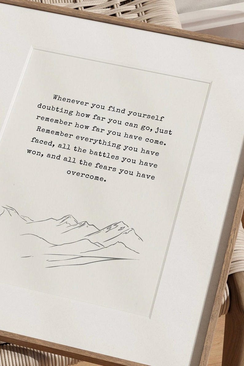May include: A motivational quote about overcoming challenges and remembering how far you've come. The quote is printed in black text on a white background with a simple line drawing of mountains at the bottom.