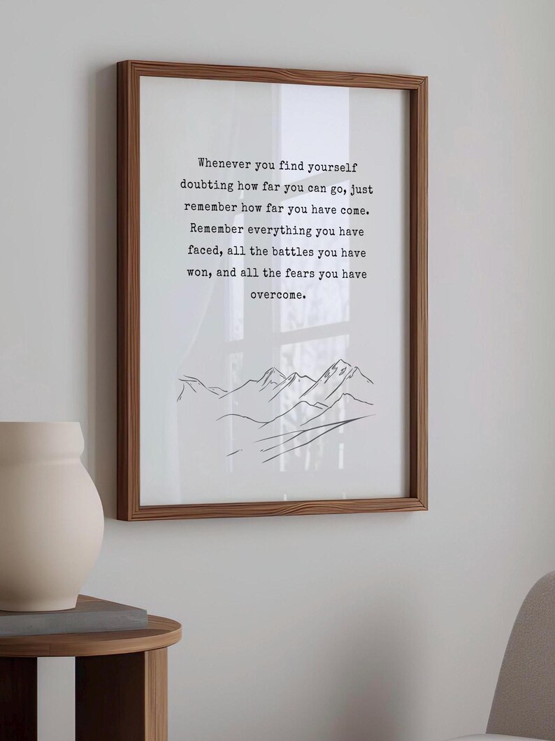 May include: A framed print with a motivational quote about overcoming challenges. The quote reads: "Whenever you find yourself doubting how far you can go, just remember how far you have come. Remember everything you have faced, all the battles you have won, and all the fears you have overcome." The print features a simple line drawing of mountains.