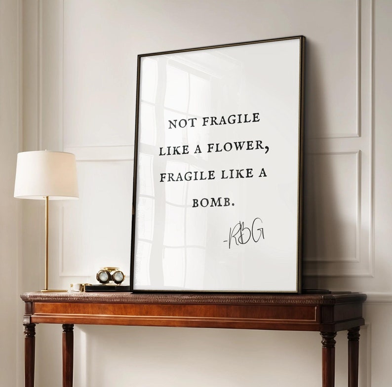 May include: Black and white framed print with a quote by Ruth Bader Ginsburg: "Not fragile like a flower, fragile like a bomb."