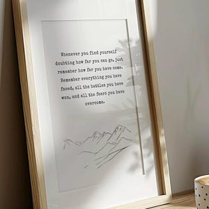 May include: A framed print with a motivational quote about overcoming challenges. The quote reads: "Whenever you find yourself doubting how far you can go, just remember how far you have come. Remember everything you have faced, all the battles you have won, and all the fears you have overcome." The print features a simple line drawing of mountains.