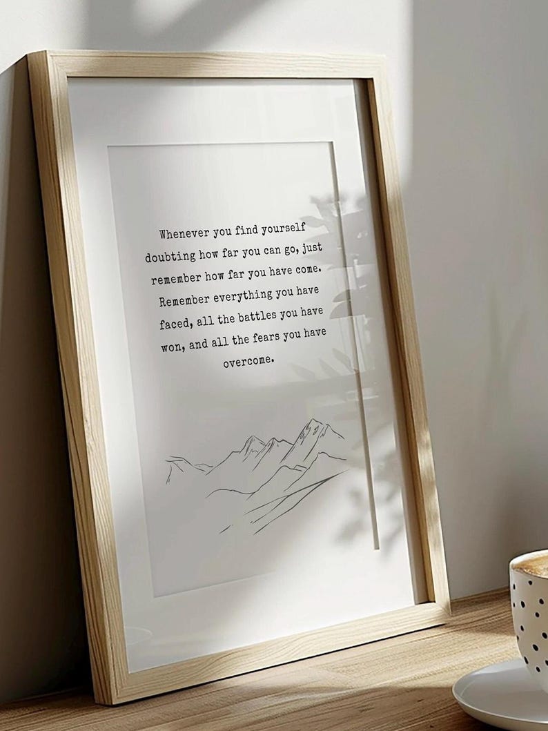May include: A framed print with a motivational quote about overcoming challenges. The quote reads: "Whenever you find yourself doubting how far you can go, just remember how far you have come. Remember everything you have faced, all the battles you have won, and all the fears you have overcome." The print features a simple line drawing of mountains.