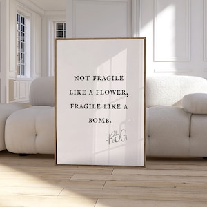 May include: A framed print with a white background and black text that reads "Not fragile like a flower, fragile like a bomb." The text is attributed to "RBG".