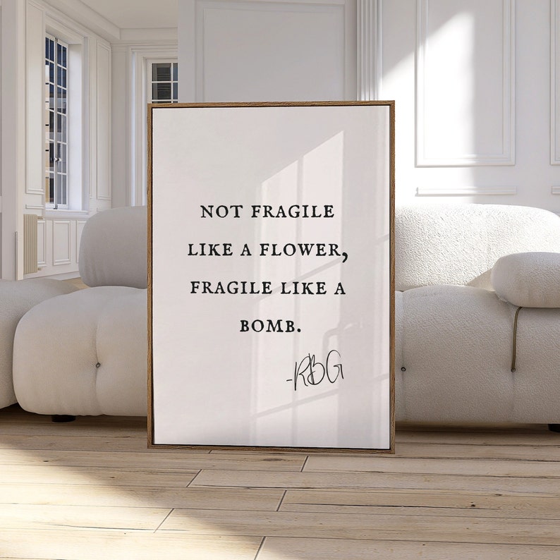 May include: A framed print with a white background and black text that reads "Not fragile like a flower, fragile like a bomb." The text is attributed to "RBG".