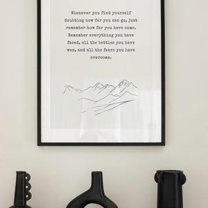 May include: A black and white inspirational quote print with a simple line drawing of mountains. The quote reads "Whenever you find yourself doubting how far you can go, just remember how far you have come. Remember everything you have faced, all the battles you have won, and all the fears you have overcome."