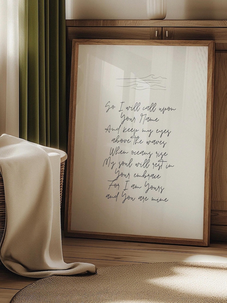 Op de afbeelding: Een witte ingelijste print met een handgeschreven gedicht over liefde en de oceaan. Het gedicht luidt: "So I will call upon Your Name And keep my eyes above the waves When oceans rise My soul will rest in Your embrace For I am Yours and You are mine"