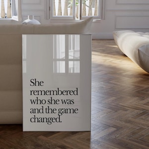 May include: A white framed poster with black text that reads "She remembered who she was and the game changed."