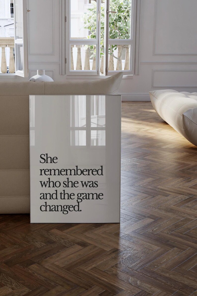 May include: A white framed poster with black text that reads "She remembered who she was and the game changed."