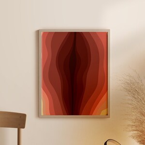 May include: Abstract art print with a layered, organic design in shades of red, orange, and yellow. The print is framed in a simple, light wood frame.