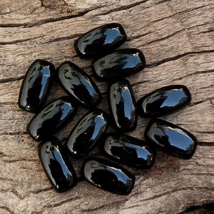 May include: A group of black oval-shaped stones on a wooden surface.