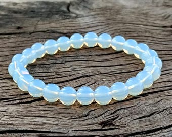 Könnte beinhalten: Ein hellblaues Perlenarmband. Das Armband besteht aus runden, opalisierenden Perlen. Die Perlen haben ein weiches, leuchtendes Aussehen. Das Armband liegt auf einer verwitterten Holzoberfläche.