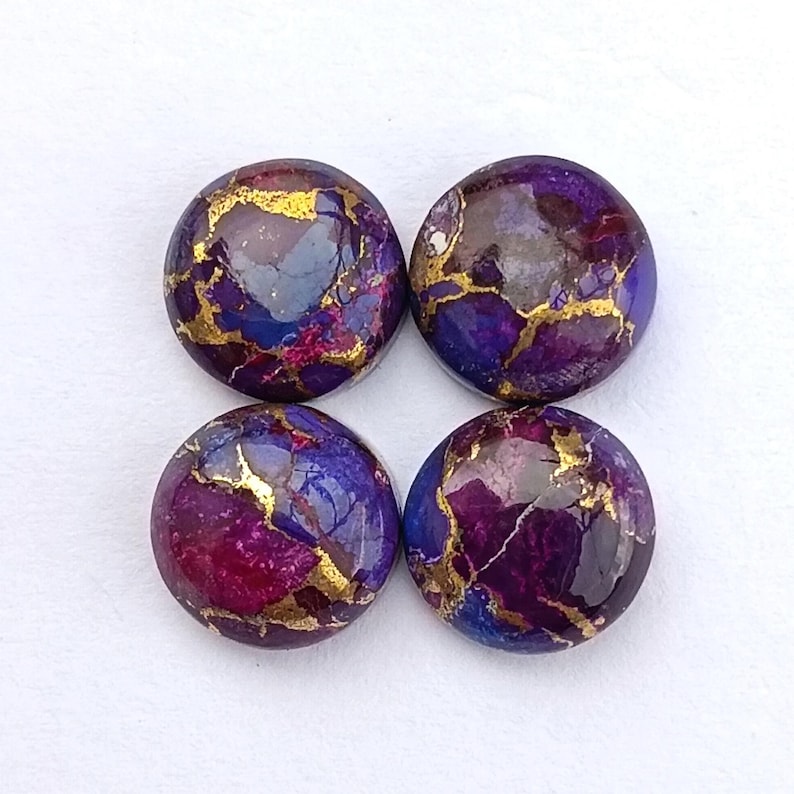 May include: Four round cabochon gemstones with a mix of purple, blue, and gold colors. The gemstones have a polished, glossy finish and are set against a white background. The stones are approximately 1 inch in diameter.