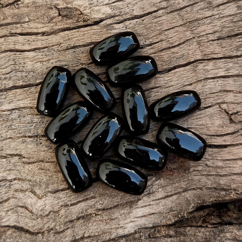 May include: A group of black oval-shaped stones on a wooden surface.