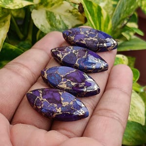 May include: Four polished, oval-shaped gemstones with a deep purple and blue base color, accented with gold veining. The stones are smooth and have a glossy finish, perfect for jewelry making or collecting.