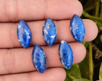 May include: Five oval-shaped lapis lazuli gemstones. The stones are a deep blue color with white and gold flecks. Each stone is approximately 1 inch long.