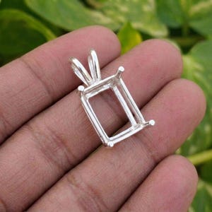 May include: A silver-colored metal pendant setting featuring a rectangular frame with four prongs at the corners designed to hold a gemstone. The setting includes a tapered bail at the top for attachment to a chain, showcasing a polished finish.