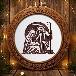 Könnte beinhalten: Ein brauner Holz-Stickrahmen mit detailliertem, geschnitztem Rand. Im Inneren zeigt ein braunes und weißes Bild die Weihnachtsgeschichte. Das Bild zeigt Maria, Josef und das Jesuskind. Der Hintergrund ist eine Holzoberfläche mit Weihnachtsdekorationen.