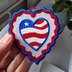 May include: A red, white, and blue embroidered heart-shaped patch with a star in the upper left corner. The heart is surrounded by a blue scalloped border.