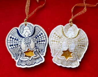 Puede incluir: Dos adornos de ángel de fieltro blanco con bordados dorados y azules. Un ángel tiene alas azules y el otro tiene alas doradas. Ambos ángeles tienen una estrella dorada en el centro.