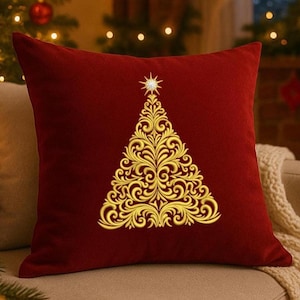May include: A square, claret velvet cushion with a gold embroidered Christmas tree design. The tree features swirling patterns and a star. The cushion is on a beige sofa, perfect for festive decor.