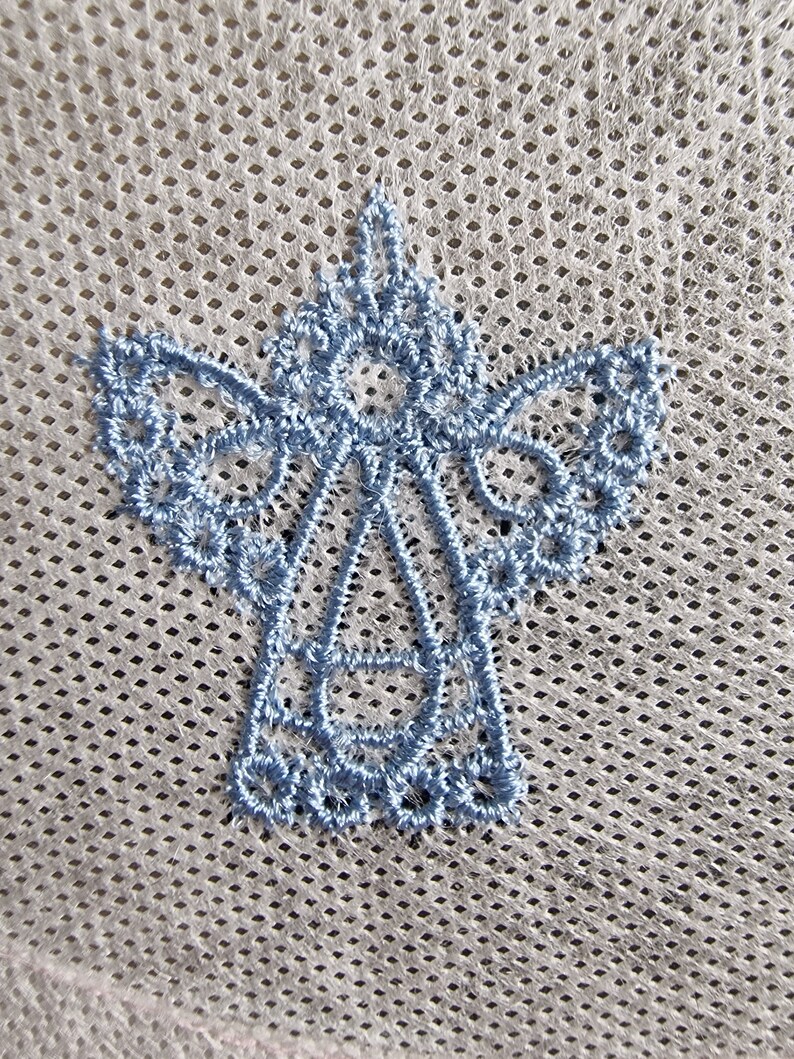 May include: A light blue embroidered angel design on a white mesh fabric.