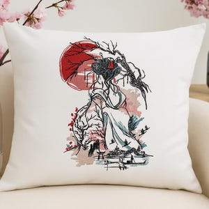 以下が含まれることがあります： 白い正方形のクッション。芸者、赤い太陽、日本の風景の刺繍デザイン。デザインは黒、赤、青。クッションは白いソファの上にあり、花瓶にピンクの花が飾られています。