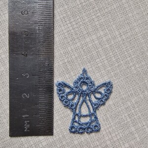 May include: A light blue embroidered angel ornament. The angel is about 2 inches tall and has a delicate lace design.