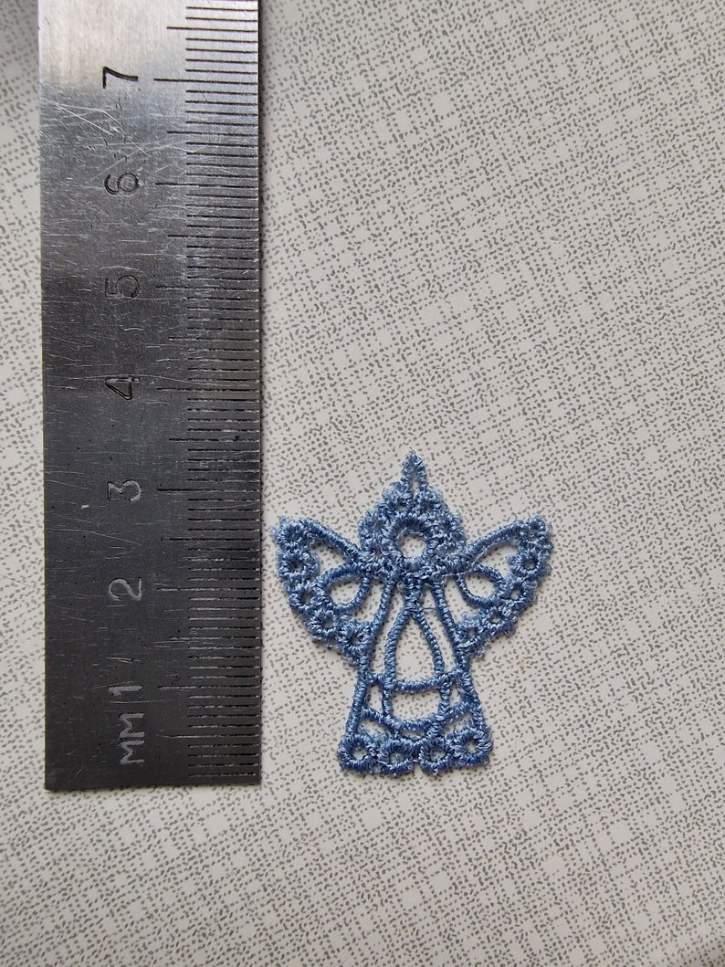 May include: A light blue embroidered angel ornament. The angel is about 2 inches tall and has a delicate lace design.
