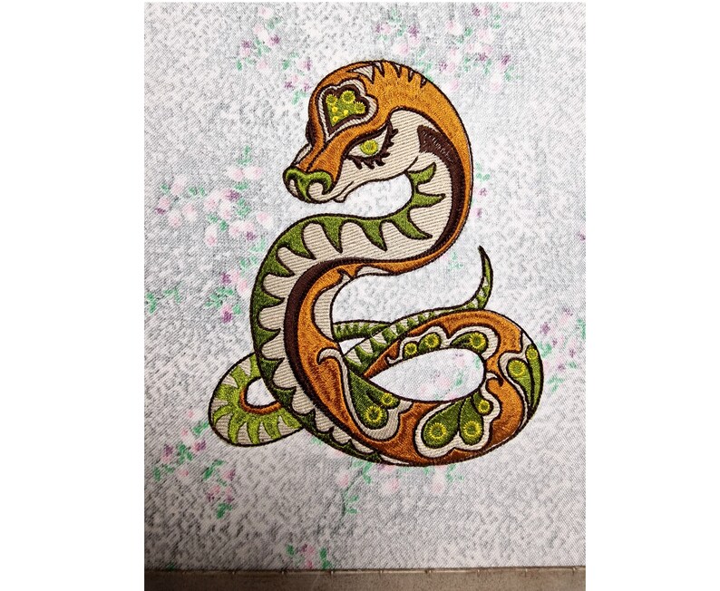 Puede incluir: Dise&ntilde;o bordado de una serpiente verde y naranja con detalles intrincados. La serpiente est&aacute; enroscada en forma de espiral con la cabeza mirando al espectador.