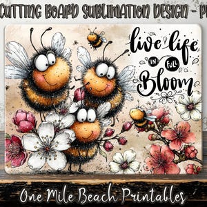 May include: A rectangular cutting board design, 40.6 x 30.5 cm, with cartoon bees and flowers. The phrase "live life in full bloom" is written in script. The design features a whimsical style. The design is by One Mile Beach Printables.