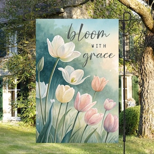 May include: A garden flag with a watercolor design of white and pink tulips. The text "bloom with grace" is written in a script font on the flag.