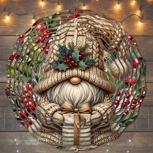 Peut inclure: Un mobile de vent en métal sur le thème de Noël représentant un gnome portant un bonnet tricoté avec du houx et des baies. Le gnome tient une boîte cadeau avec un nœud. L'arrière-plan est un motif tourbillonnant de feuilles vertes et de baies rouges.