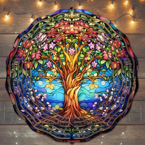 May include: A colorful stained glass tree of life wind chime with a blue, green, and purple background. The tree has a brown trunk and branches with pink, red, and yellow flowers. The wind chime is made of metal and has a circular shape.