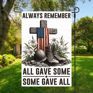 May include: A white garden flag with a wooden cross, an American flag, and military boots. The text on the flag reads "Always Remember All Gave Some Some Gave All".