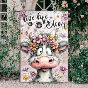 May include: A garden flag featuring a cartoon cow with a floral crown and the text "live life in full bloom." The cow has a pink nose and is surrounded by colorful flowers. The flag is designed for outdoor use.