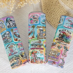 May include: Three colorful stainless steel tumblers with a summer beach theme. Each tumbler features a skeleton graphic with different summer-themed phrases like "Suns Out Bones Out" and "Beach Hair Don't Care".