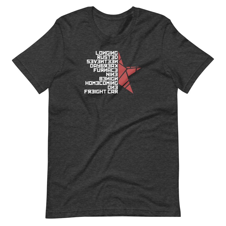 May include: Dark gray t-shirt featuring a red star design and white text. The text includes words like "Longing", "Rusted", and "Freight Car". The shirt is made of a soft material and has a classic crew neck.